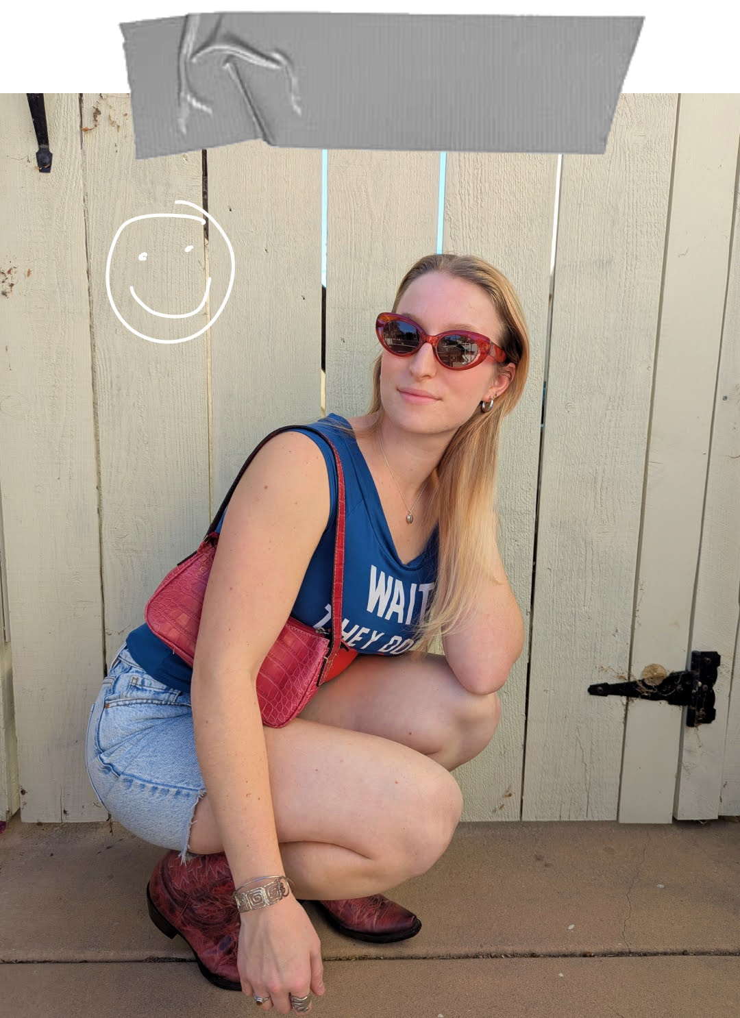 Grace, a white woman with blond hair, crouches down and smiles for a photo. She is wearing a navy blue top with light wash denim shorts, plus red cowboy boots, a red purse, and red sunglasses. A smiley face is drawn in white ink in the top left corner of the photo.